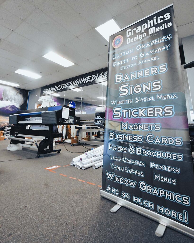 interior wide angle photo of our las vegas large format print shop with a retractable banner in foreground and one of our printers in the background with orders going out sitting in between them